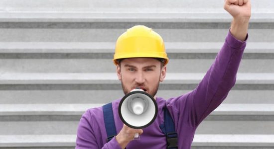 Protesting young man shouting into megaphone against metal fence