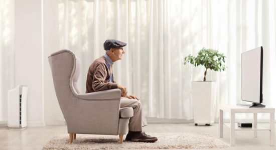 Elderly man sitting in an armchair and watching tv at home