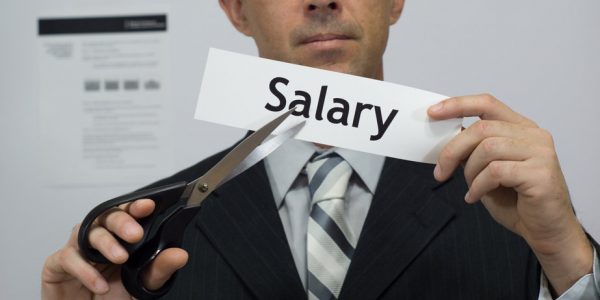 Male office worker or businessman in a suit and tie cuts a piece of paper with the word salary on it as a salary or pay reduction business concept.